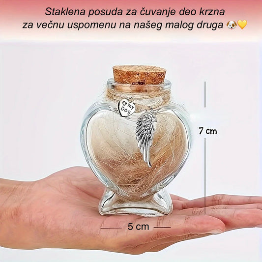 Heart-shaped glass jar with angel wing charm and hair lock, held in a hand for scale.