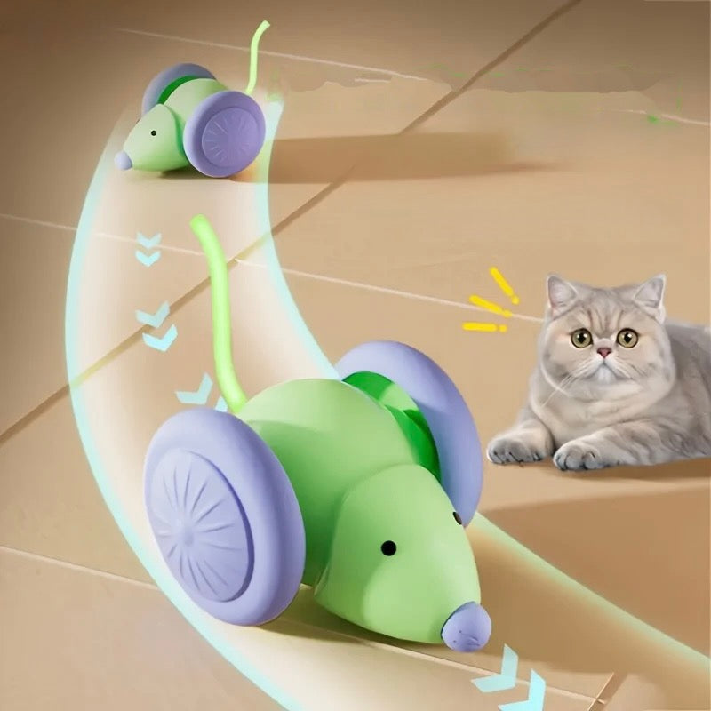 Green and purple toy mouse with wheels on a beige floor, cat looking at it.