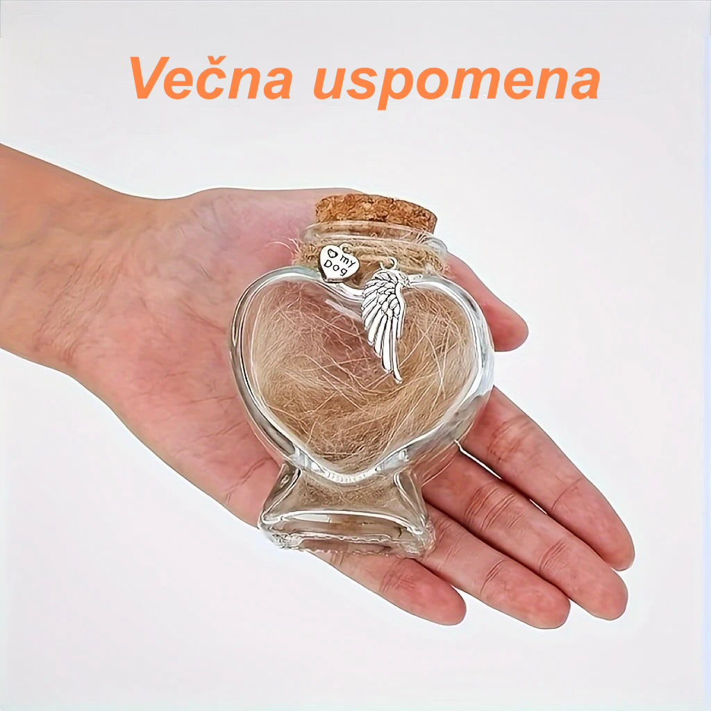 Heart-shaped glass jar with hair and angel wing charm held in a hand, against a light background.