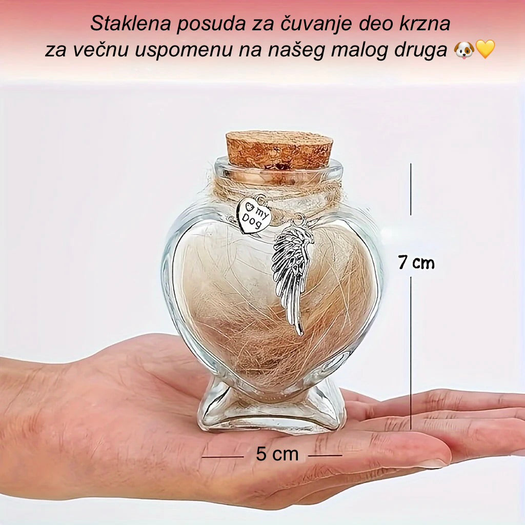 Heart-shaped glass jar with angel wing charm and hair lock, held in a hand for scale.